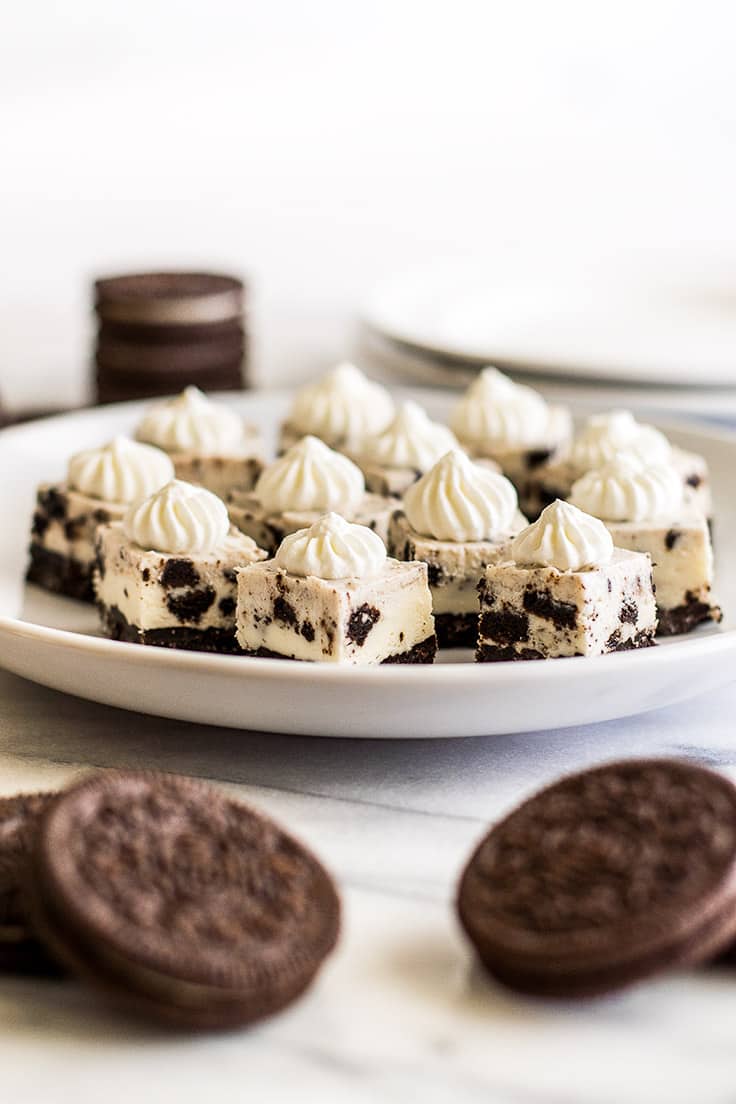 Oreo cheesecake bites with whipped cream on a white plate.