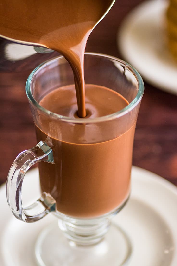 Thick hot chocolate being poured into a glass mug.