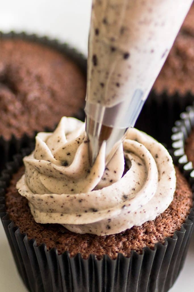 Oreo frosting being piped on a chocolate cupcake.