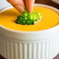 Piece of broccoli being dipped in cheese sauce.