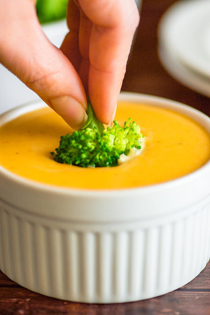 Photo of broccoli being dipped in creamy cheese sauce.