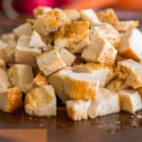 Cooked chicken breasts cubed on a cutting board.