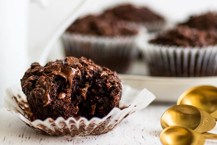 The BEST Chocolate Banana Muffins you'll ever eat. This easy small-batch recipe makes 5 muffins. You just need one ripe banana and one bowl, and you can be pulling these out of your oven in less than half an hour. | #breakfast | #chocolate | #bananamuffins | #breakfastfortwo | Wide photo of Small-batch Chocolate Banana Muffin with a bite out of it in front of a white mug.