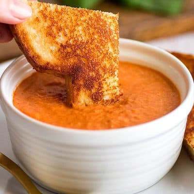 Photo of grilled cheese sandwich being dipped in Creamy Tomato Soup Recipe for Two.