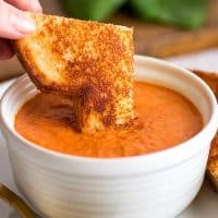 Square photo of grilled cheese sandwich being dipped in Creamy Tomato Soup Recipe for Two.