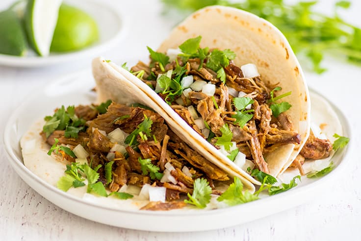 Three classic carnitas tacos, pork tacos with cilantro and diced onion.
