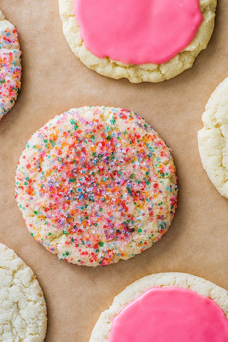Small-batch Sugar Cookies rolled in rainbow sprinkles and glazed on parchment paper.
