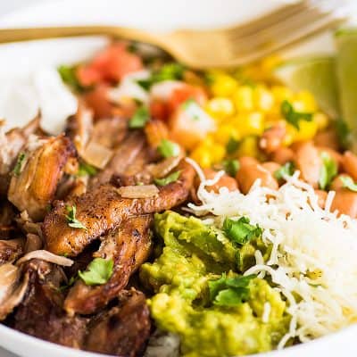 Photo of a Carnitas Burrito Bowl in a white bowl with carnitas, cheese, corn, and guacamole.