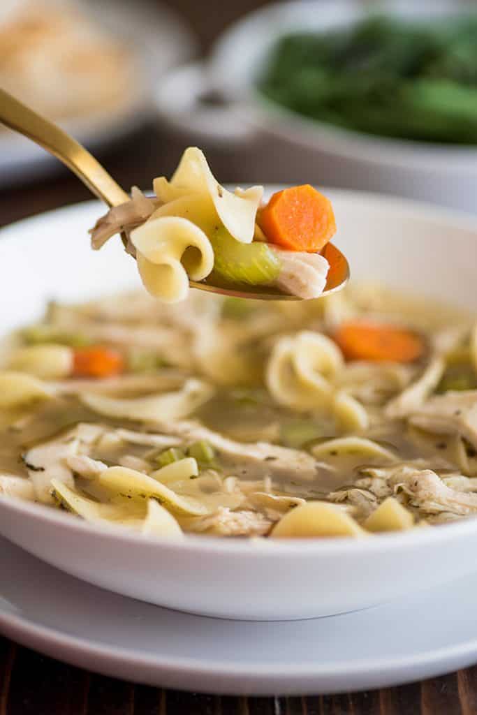Photo of a spoonful of Easy Chicken Carcass Soup in a white bowl.