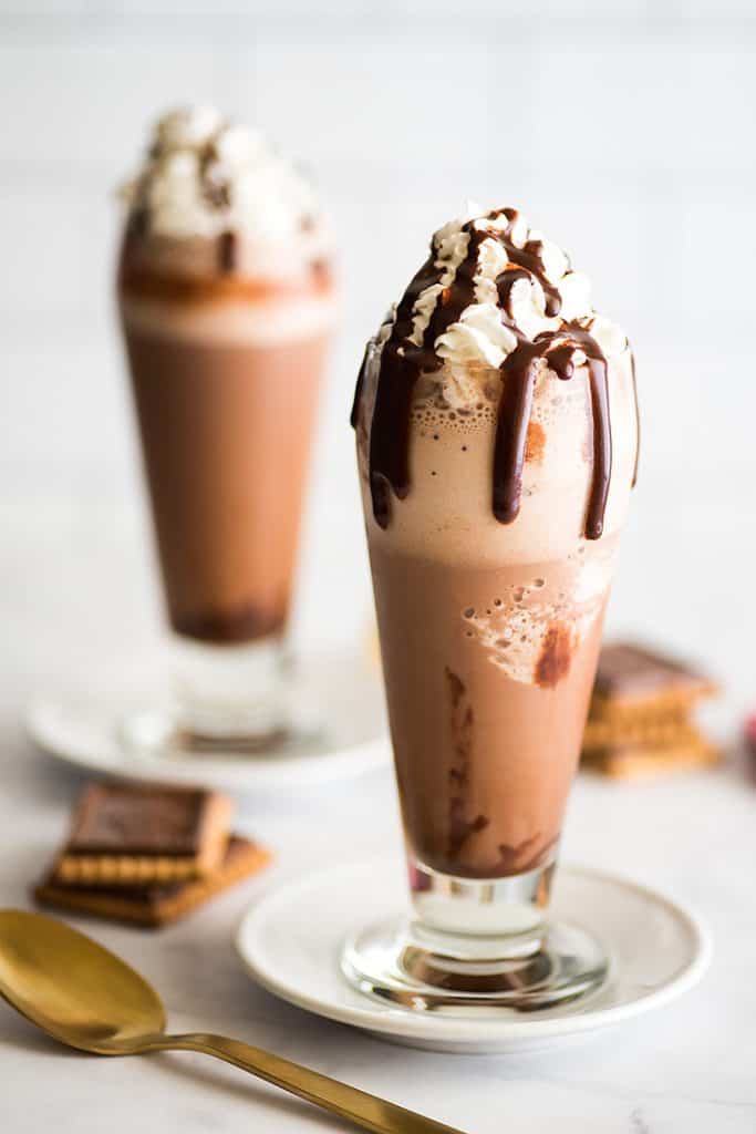 Image of two cups of frozen hot chocolate with whipped cream and chocolate fudge sauce drizzle.