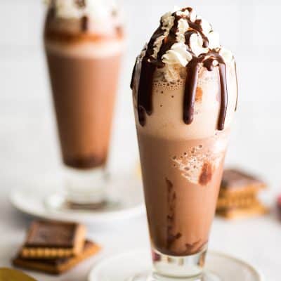 Image of two cups of frozen hot chocolate with whipped cream and chocolate fudge sauce drizzle.