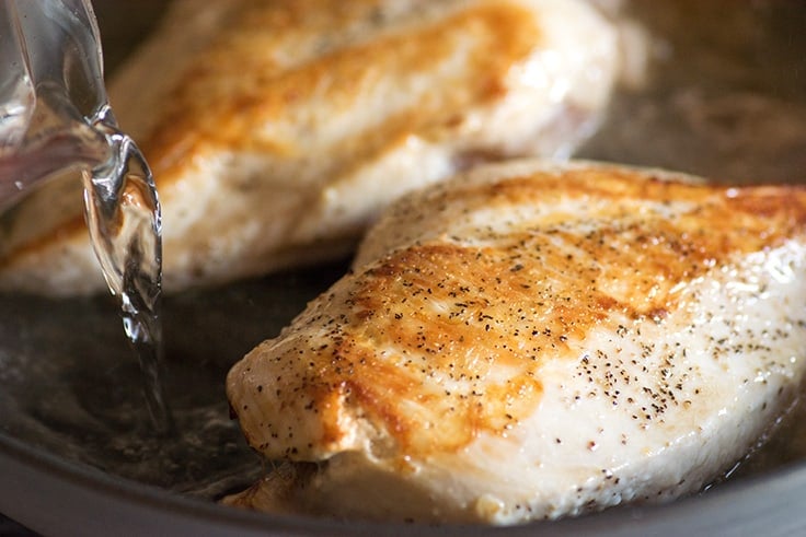 Water being added to a pan of cooking chicken.