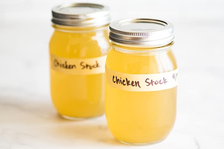 Photo of two jars of homemade chicken stock on white counter.
