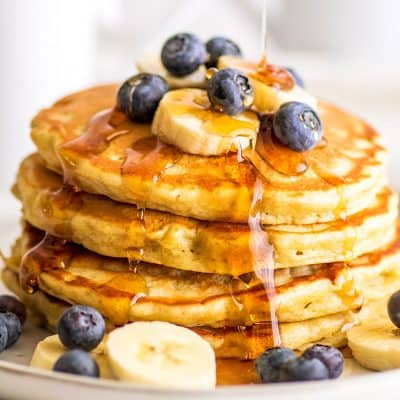 Stack of Easy Banana Pancakes for Two topped with blueberries and banana slices being drizzled with syrup.