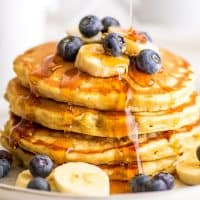 Stack of Easy Banana Pancakes for Two topped with blueberries and banana slices being drizzled with syrup.