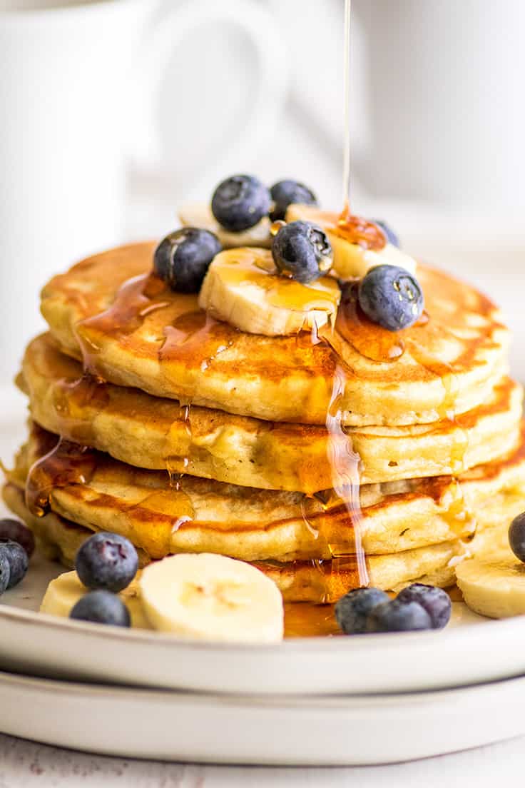 Stack of small-batch banana pancakes topped with blueberries and banana slices being drizzled with syrup.