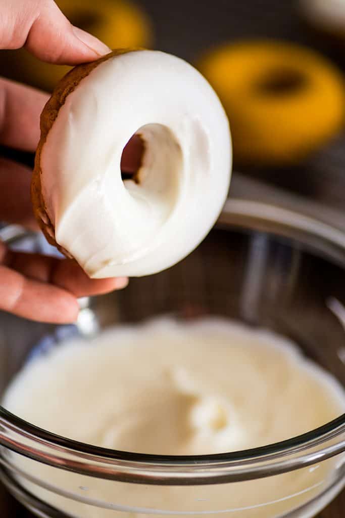 Photo of a baked pumpkin donut being dipped in cream cheese glaze.