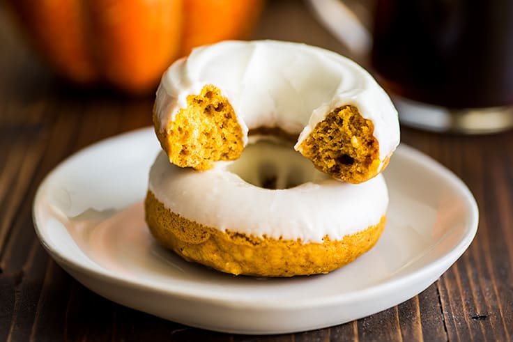 One-and-a-half baked pumpkin donuts with cream cheese frosting stacked on a plate.