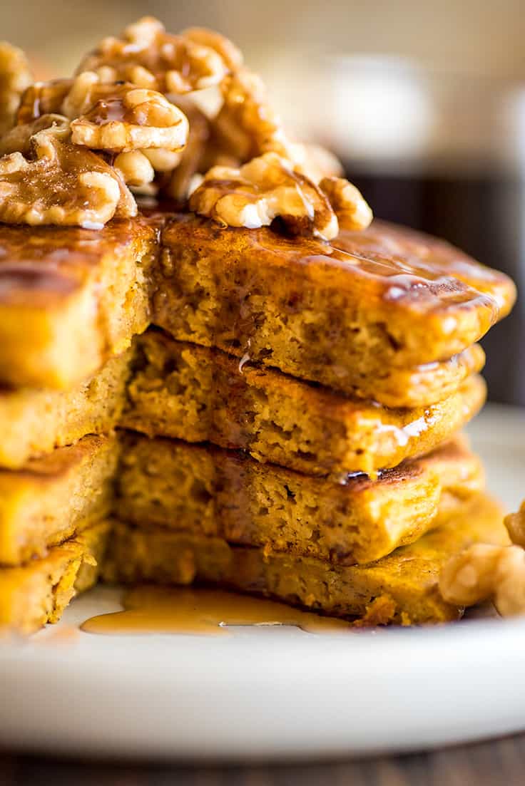 Close up photograph of a stack of pumpkin pancakes with a piece cut out of it.