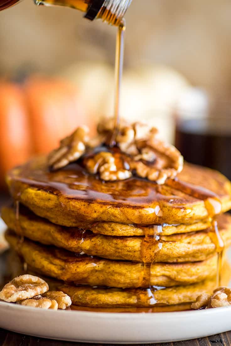 Photograph of syrup being poured over a stack of pumpkin pancakes.