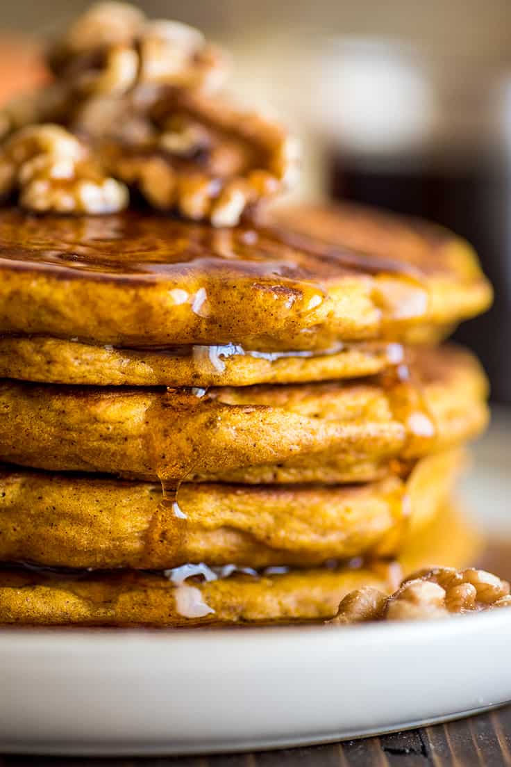 Close up photo of stack of Pumpkin Pancakes for Two on a white plate with syrup dripping down the side.
