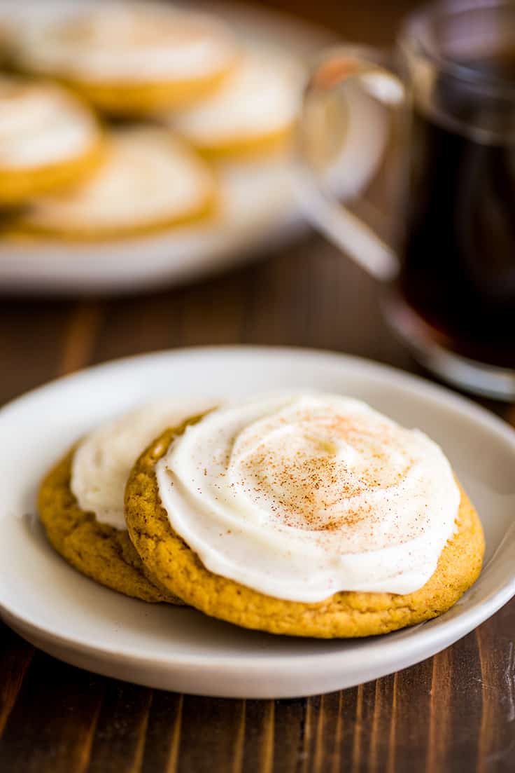 Two pumpkin cookies with cream cheese frosting on a white plate.