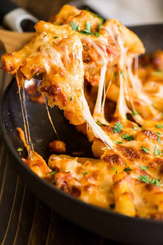 Photo of a scoop of baked ziti with melted cheese.