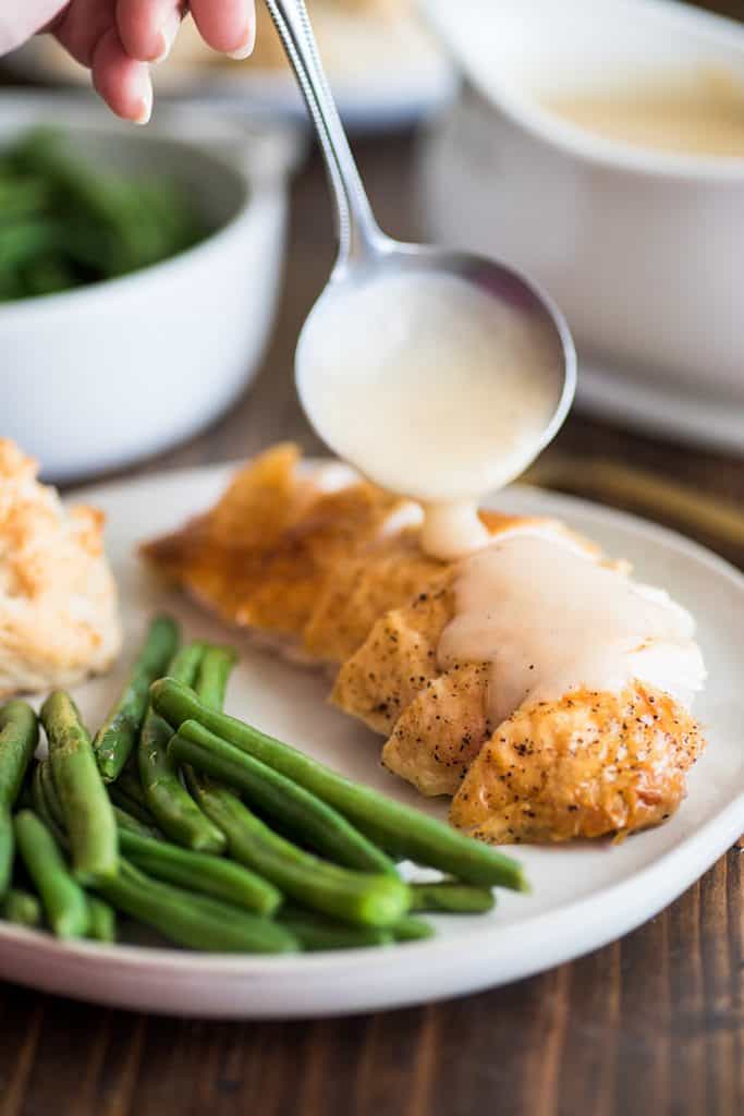 Photo of gravy made from pan drippings being spooned over roasted chicken breast.
