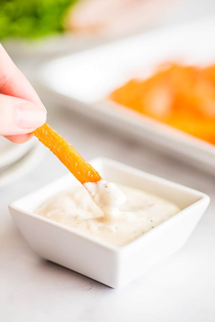 Photo of a sweet potato fry being dipped in a small batch of garlic aioli.