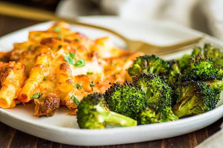 Image of crispy oven-roasted broccoli on a plate with baked ziti.