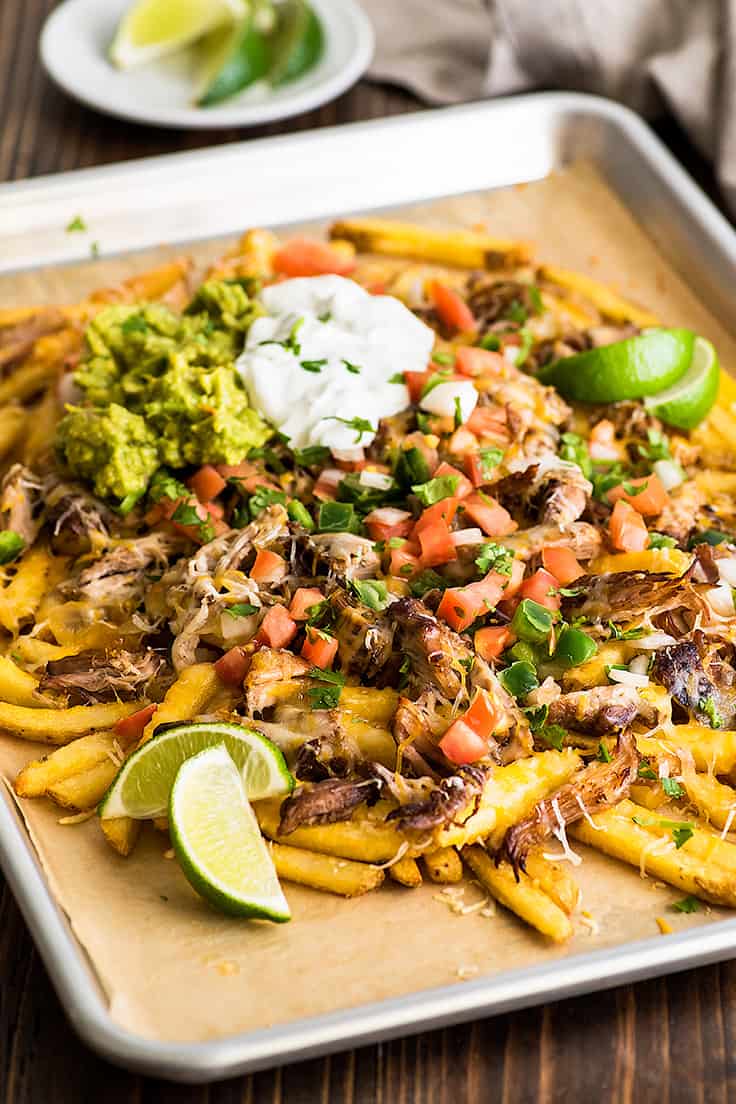 Image of Carnitas Nacho Fries on a baking sheet with sour cream and guacamole.