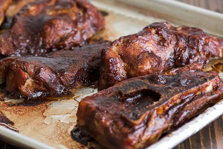 Country-style pork ribs in the oven are the perfect easy dinner. Cheap, easy to make, and SO good, this might be your new favorite way to eat pork. | cheap meals | BBQ | #summer | #summerrecipes | Photo of country-style pork ribs step 4, ribs on a tray with baked on BBQ sauce.