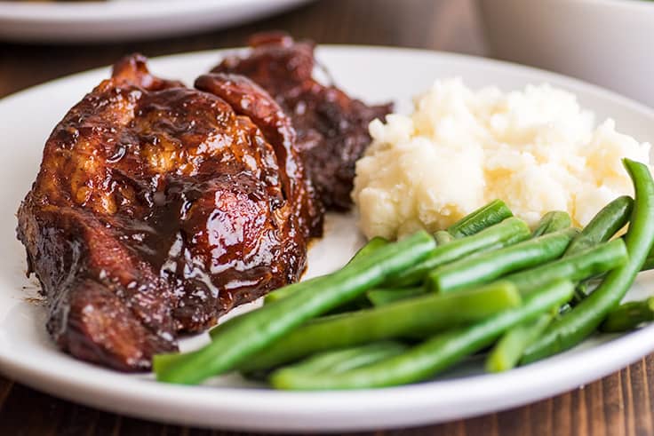 Country-style pork ribs in the oven are the perfect easy dinner. Cheap, easy to make, and SO good, this might be your new favorite way to eat pork. | cheap meals | BBQ | #summer | #summerrecipes | Picture of baked country-style pork ribs on a plate with green beans and mashed potatoes.