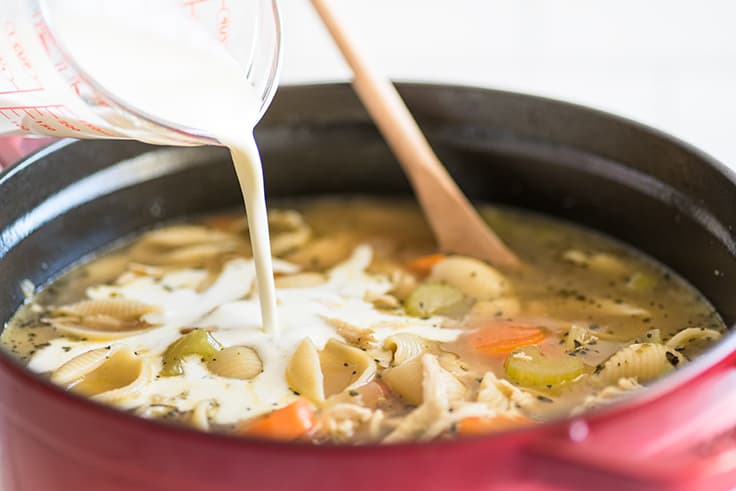 Photo of Easy Creamy Chicken Noodle Soup in a pot with heavy cream being added.