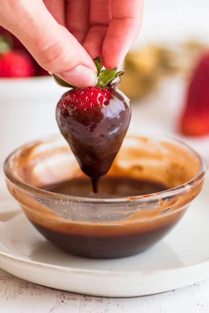 This Nutella sauce is so easy to make! Two ingredients, 30 seconds, and perfect for drizzling over ice cream, pancakes, and waffles. | #summerdessert | #Nutella | #recipeforone | recipes for one | Photo of a strawberry being dipped in Nutella sauce.