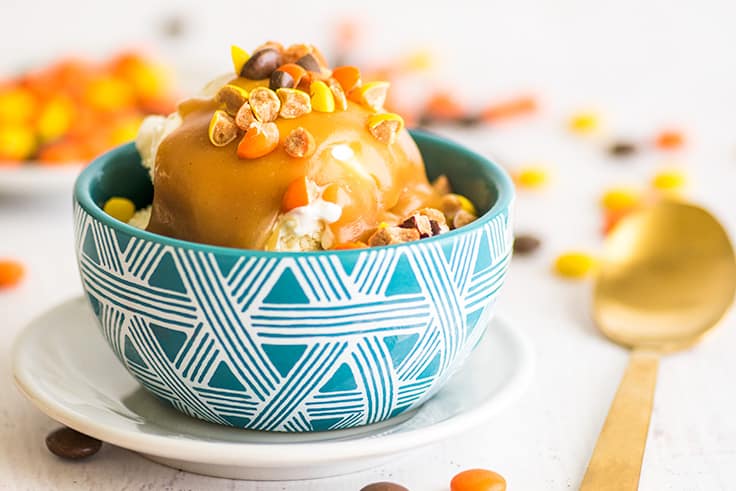 Love this peanut butter sauce! Two ingredients and 30 seconds are all you need to make this single-serving peanut butter sauce for ice cream, pancakes, or waffles. | #summerdessert | #peanutbutter | #recipeforone | recipes for one | Wide photo of peanut butter sauce in a blue bowl with chopped up Reese's Pieces on top.