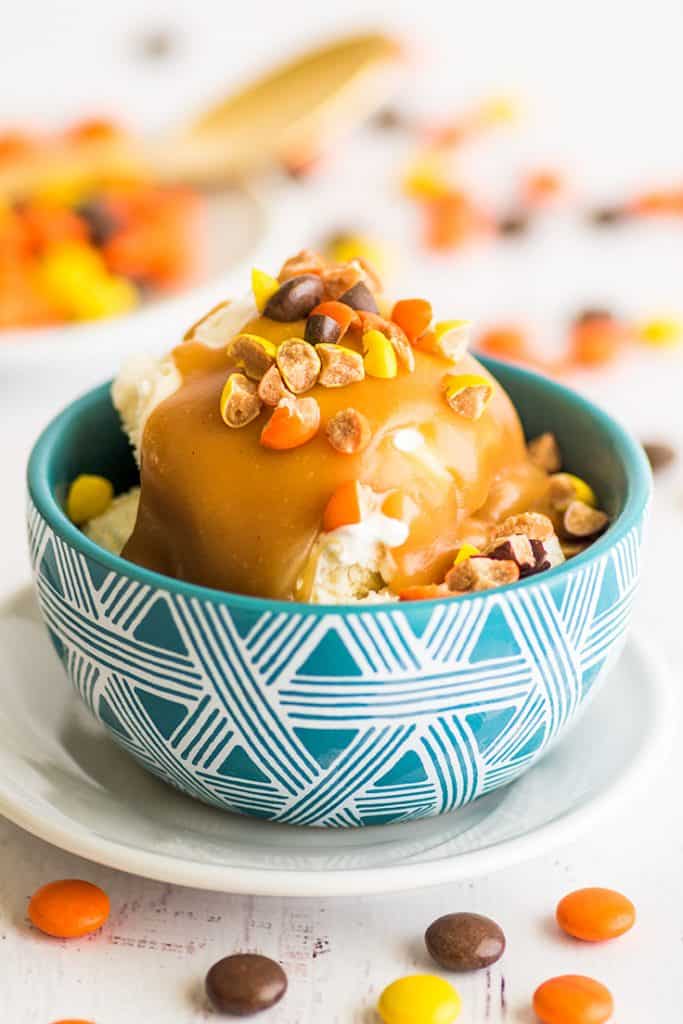 Love this peanut butter sauce! Two ingredients and 30 seconds are all you need to make this single-serving peanut butter sauce for ice cream, pancakes, or waffles. | #summerdessert | #peanutbutter | #recipeforone | recipes for one | Photo of peanut butter sauce over ice cream in a blue bowl with chopped up Reese's Pieces on top.