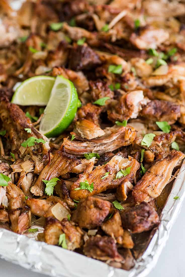 Crispy Slow Cooker Carnitas on a baking tray with lime slices and cilantro.