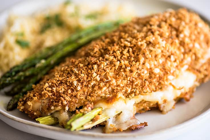 Image of asparagus-stuffed chicken breast on a white plate with orzo and roasted asparagus.