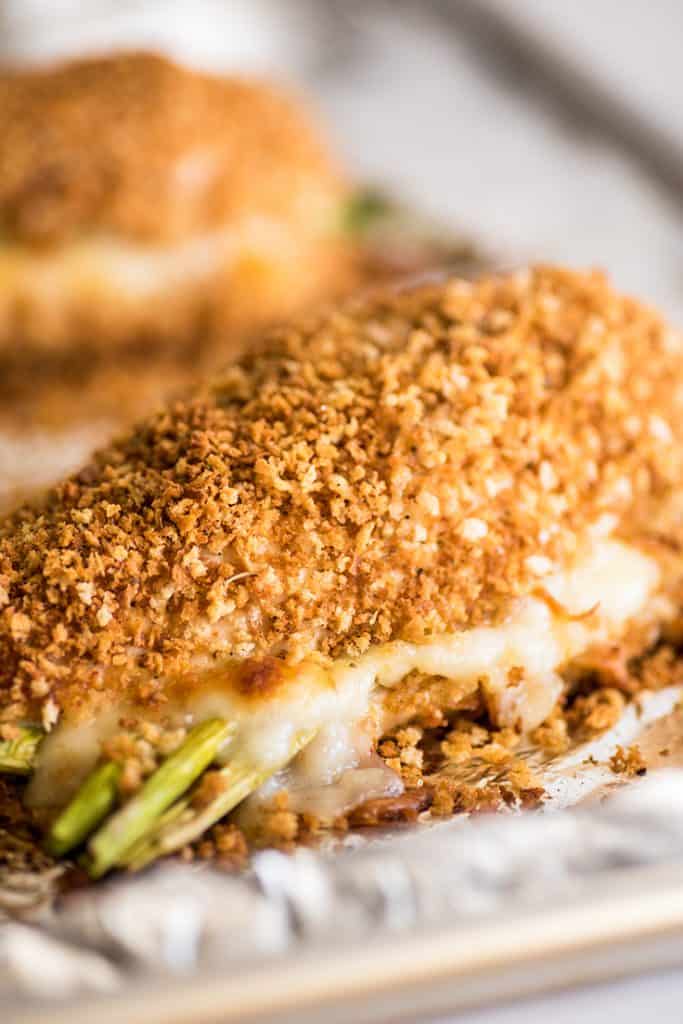 Photo of asparagus stuffed chicken breast filled with mozzarella on a baking sheet.