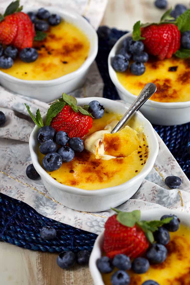 Photo of Creme Brulee recipe made with egg yolks recipe in white ramekins with fruit on top.