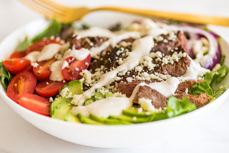 Photo of Carne Asada Salad in a white bowl with chipotle lime yogurt dressing.