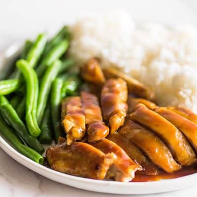 Image of chicken thighs in homemade teriyaki sauce on a plate with green beans and rice.
