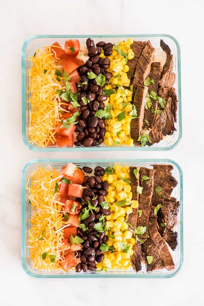 Overhead shot of two meal prep carne asada burrito bowls in glass containers.