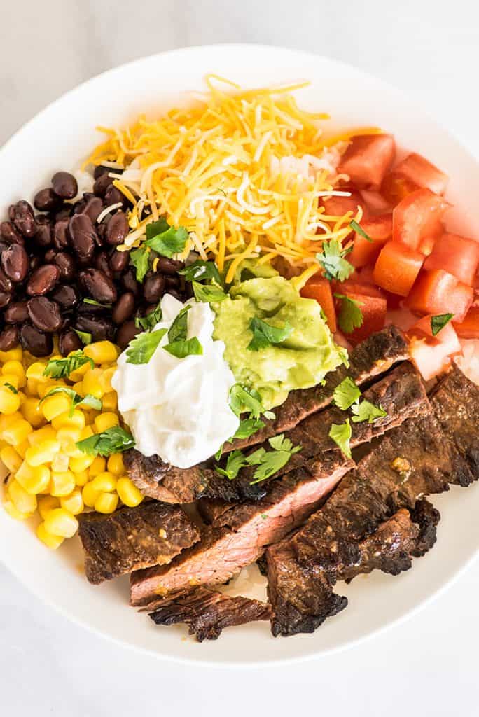 Overhead shot of carne asada burrito bowl in a white bowl on marble back drop.