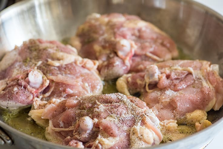 Lemon chicken thighs cooking in skillet.