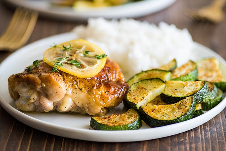 Lemon chicken thigh on plate with zucchini and rice.