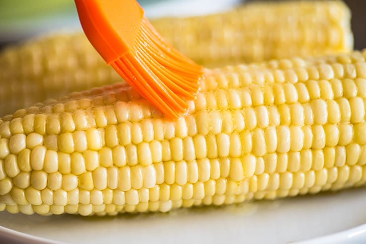 Microwaved corn on the cob being brushed with butter.