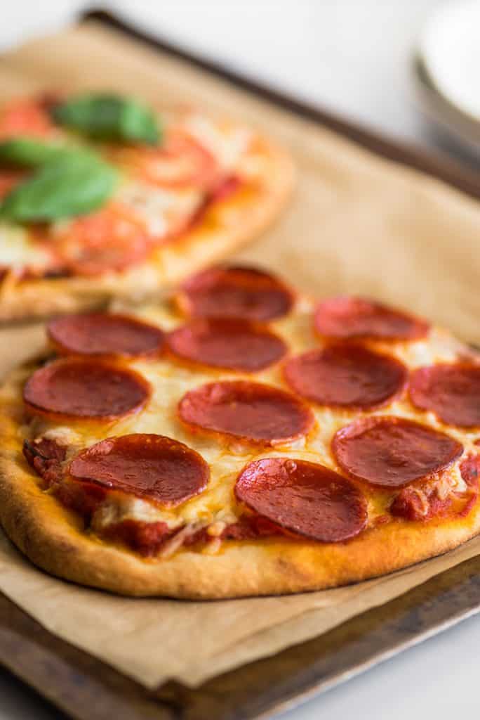 Photo of pepperoni naan pizza on a baking sheet.