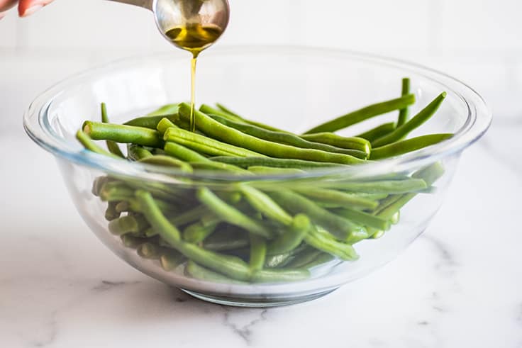 Green beans in a bowl being drizzled with olive oil.